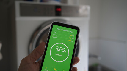 A man holds a smart phone with energy consumption app displaying energy usage in a laundry setting