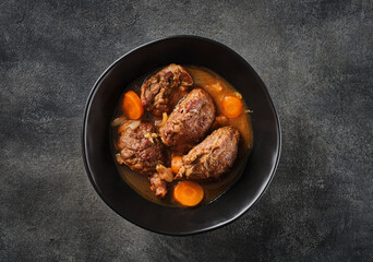 Traditional German braised pork cheeks in brown sauce with carrot as closeup.