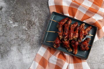 Hoisin chicken wings on wooden skewers on a rectangular  plate on a dark background. Top view, flat lay