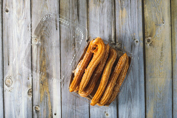 Churros in a plastic container on a wooden table.