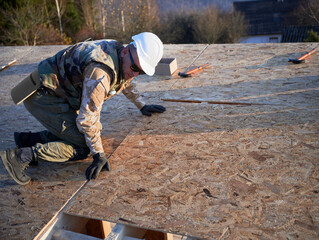 Carpenter mounting wooden OSB board on rooftop of future cottage. Man worker building wooden frame house. Carpentry and construction concept.