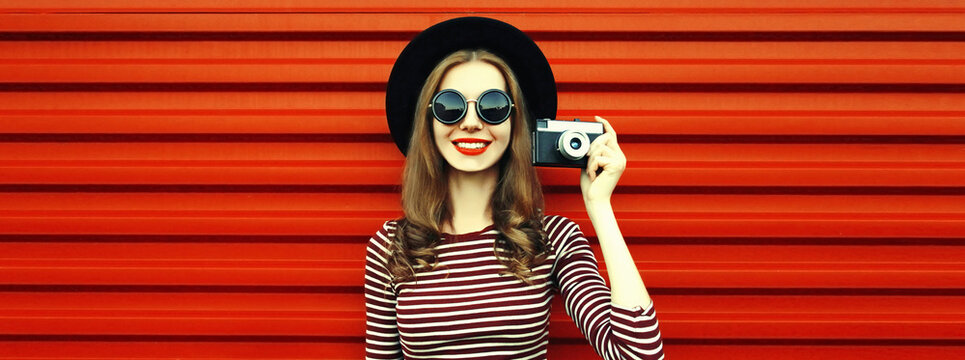 Portrait of happy smiling young woman photographer with film camera on red background