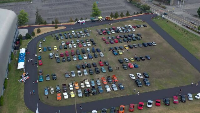 Aerial orbit of car enthusiasts that came from different towns walking around and looking and modern and classic cars on display.