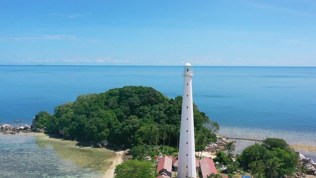 aerial of white lighthouse on remote lengkuas island with tourists in tropical blue water of belitung indonesia