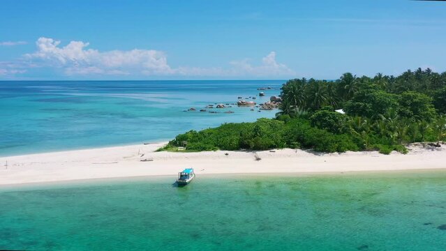 aerial zoom out of boat anchored on pristine empty white sand tropical beach in belitung indonesia on sunny summer day