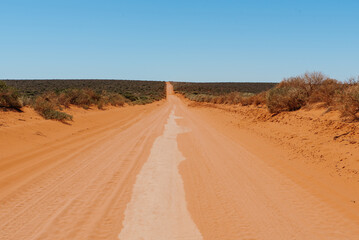 Fototapeta na wymiar Australian outback red dirt road. Remote track in Australian bushland against clear blue sky