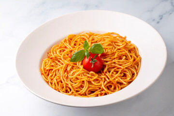 Tasty appetizing classic italian spaghetti pasta with tomato sauce, cheese parmesan and basil on plate and ingredients for cooking pasta on white marble table.