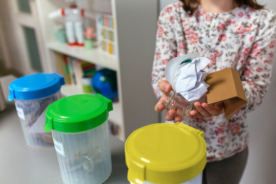 Unrecognizable Girl In Ecology Classroom Showing Handful Of Waste To Recycle With Selective Trash Bins In Foreground