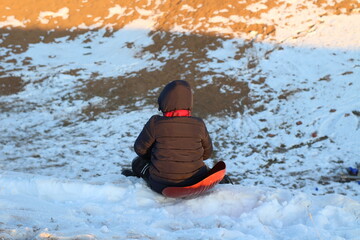 Fototapeta na wymiar Kid sledding on snow in winter