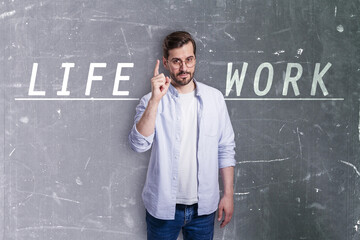 Attractive young european man in glasses and with writing on concrete wall pointing up and trying to balance life and work. Success, career, failure, work, life and personal development concept.