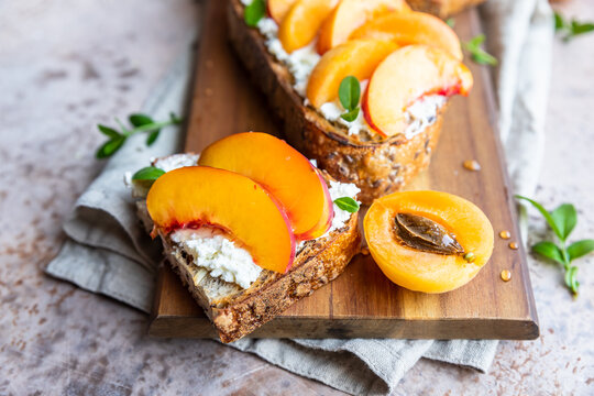 Open sandwiches with tartine bread and cream cheese, nectarine and apricot drizzled with honey on wooden board. Concrete background.