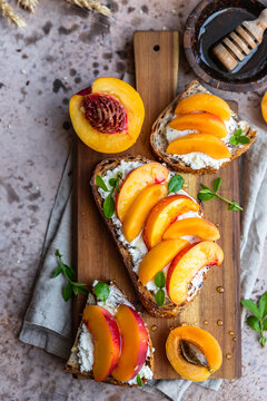Open sandwiches with tartine bread and cream cheese, nectarine and apricot drizzled with honey on wooden board. Concrete background.