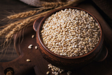 Bowl of dry raw broken pearl barley cereal grain on dark wooden background. Cooking pearl barley...