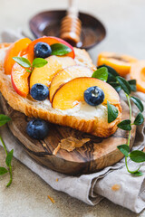 Vegetarian croissant sandwiches with nectarine, soft or cream cheese, blueberries and honey on concrete background. Healthy breakfast or lunch.