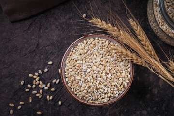 Bowl of dry raw broken pearl barley cereal grain on dark background. Cooking pearl barley porridge...