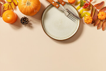 Autumn Halloween or Thanksgiving day table setting. Autumn background with an empty plate, cutlery, pumpkins. Thanksgiving background mock up. View from above. Copy space.