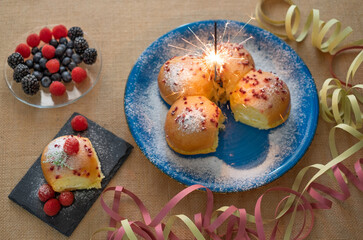 Home cooking concept. Fresh organic homemade sweet soft milk bread filled with cream and decorated with berries, on blue dish with sparkling lights