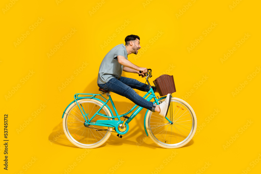 Sticker Side profile photo of young active energetic man driving new retro bicycle legs up crazy hurry fast speed look empty space isolated on yellow color background