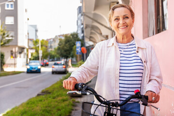 Obraz premium Beautiful happy caucasian active senior woman with bike in summer city, active pensioner lifestyle