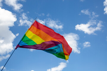 Regenbogenflagge vor blauem Himmel mit Wolken bei einer Parade zum CSD	
