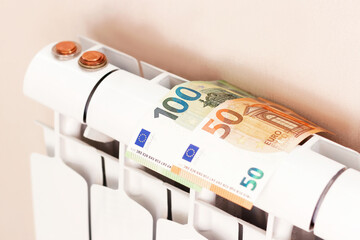 Euro money banknotes and coins on heating radiator battery. Concept of expensive heating costs and rising energy bill prices for winter cold season in Europe