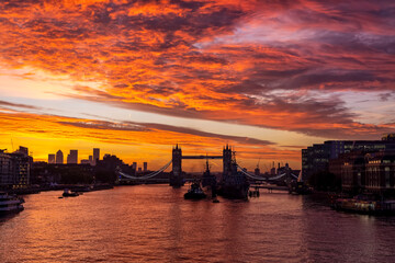 Naklejka premium A intense, red sunrise behind the skyline of London, England, with the famous Tower Bridge and River Thames