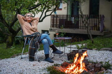 Beautiful elderly happy woman pensioner enjoying the evening sitting by the fire place in the...