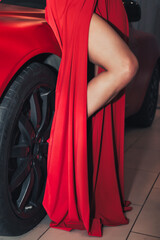 Close up leg young woman model at present car, newly automobile at dealership. Woman in red dress with new automobile with luxury auto shop. Car presents concept. Copy text space