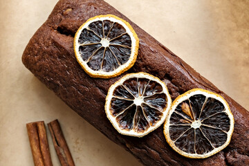 Homemade chocolate roll on baking paper with a cinnamon stick and a slice of dried orange. Top view, close-up.