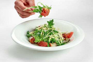 Hand takes an eel and grapefruit salad from a white plate on a white tablecloth. Close-up, selective focus