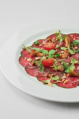 Veal carpaccio with spices and oil on a white plate on a white tablecloth. Close-up, selective focus