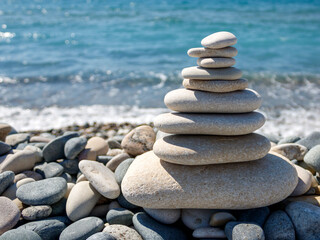 Zen stone pyramid on the beach in front of blurred blue sea wave