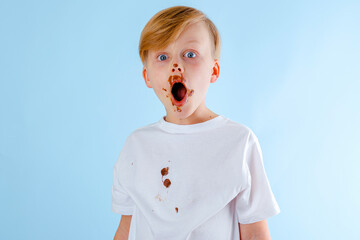 Cute surprised boy with chocolate on his face and clothes, looking in the camera. isolated. on a...