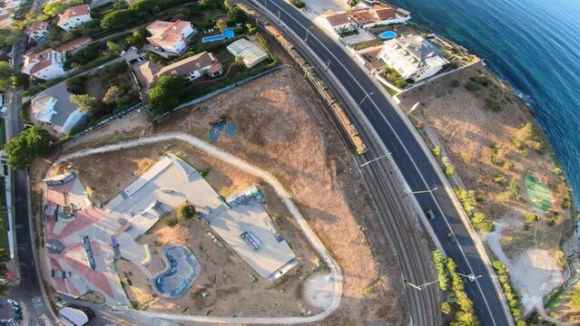 side wide drone shot of Skatepark Parque das Gera&ccedil;&otilde;es in Cascais Portugal. revealing the empty skate park with training crossing enjoying a wonderful sunrise with amazing orange sunset colors. Estoril