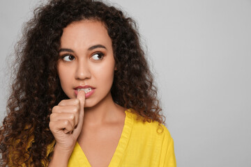 Fototapeta na wymiar African-American woman biting her nails on grey background. Space for text