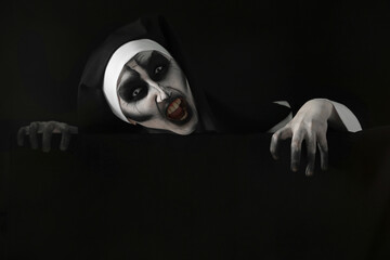 Portrait of scary devilish nun on black background. Halloween party look