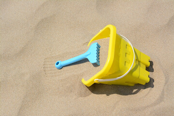 Fototapeta na wymiar Plastic bucket and rake on sand, space for text. Beach toys