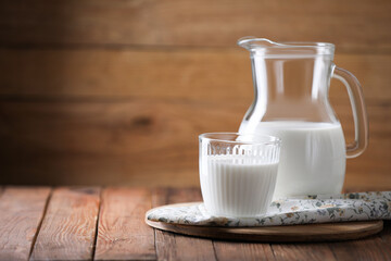 Tasty fresh milk in jug and glass on wooden table, space for text