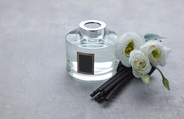 Reed sticks, glass bottle with aromatic liquid and eustoma flowers on gray marble table