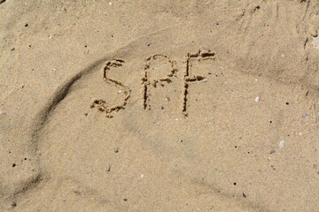 Abbreviation SPF written on sand at beach, top view. Space for text
