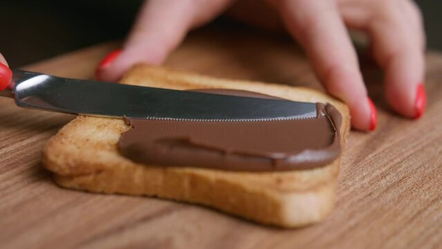 Spreading creamy chocolate over toasted bread with knife. Macro shot