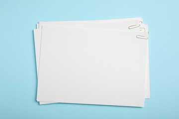 Sheets of paper with clips on light blue background, top view