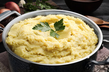 Pot of tasty mashed potatoes with parsley on black wooden table, closeup
