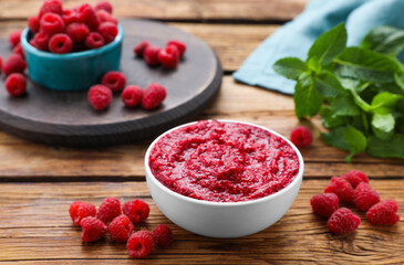 Raspberry puree in bowl and fresh berries on wooden table