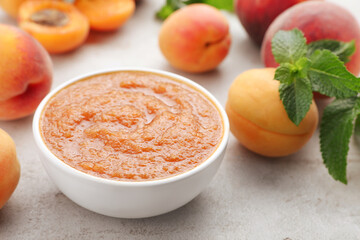 Apricot puree in bowl and fresh fruits on light grey table, closeup