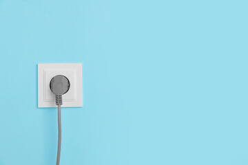 Power socket with inserted plug on light blue wall, space for text. Electrical supply
