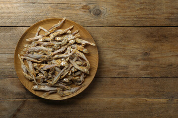 Fototapeta na wymiar Delicious dried anchovies on wooden table, top view. Space for text