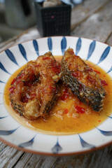 Fried fish with chilli in a ceramic plate on an old wooden floor. The taste is sour, sweet and slightly spicy.