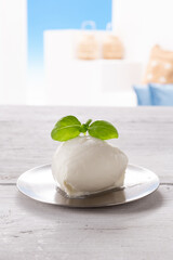 mozzarella with basil leaf on round silver plate, resting on white wooden table