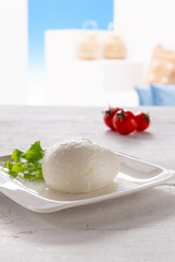 mozzarella with tomato and salad leaf on white square plate, resting on white wooden table